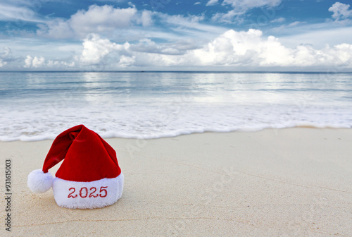 Fototapeta Naklejka Na Ścianę i Meble -  New Year 2025 background with red Santa hat on Caribbean beach.