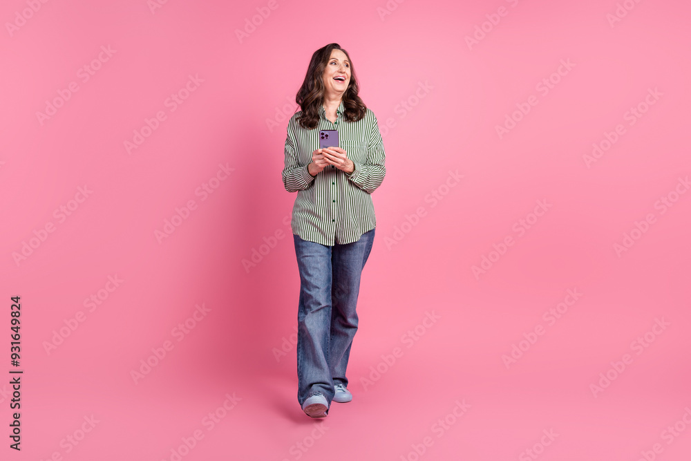 Full size photo of nice aged woman walk phone look empty space wear shirt isolated on pink color background Full size photo of nice aged woman walk phone look empty space wear shirt isolated on pink color background