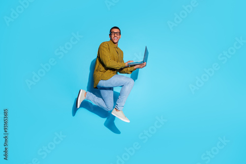 Full body photo of attractive young man jump hold netbook dressed stylish plaid clothes isolated on blue color background