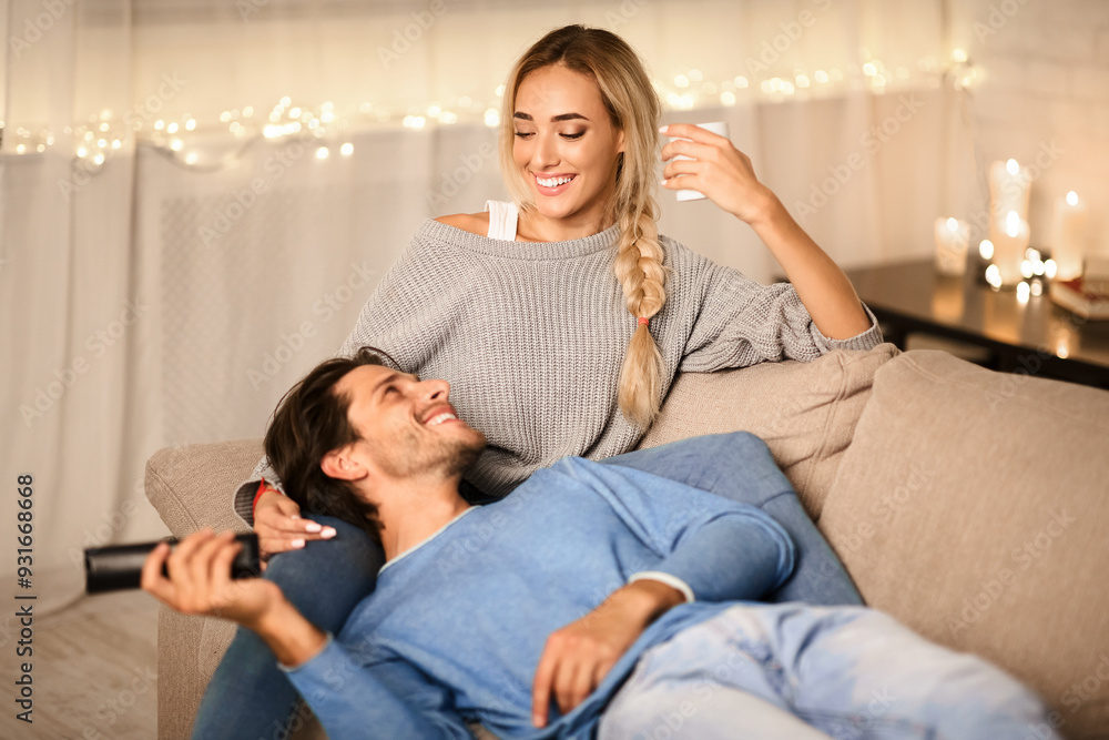 Young couple enjoying winter holidays, talking and watching tv on sofa in cozy room Young couple enjoying winter holidays, talking and watching tv on sofa in cozy room