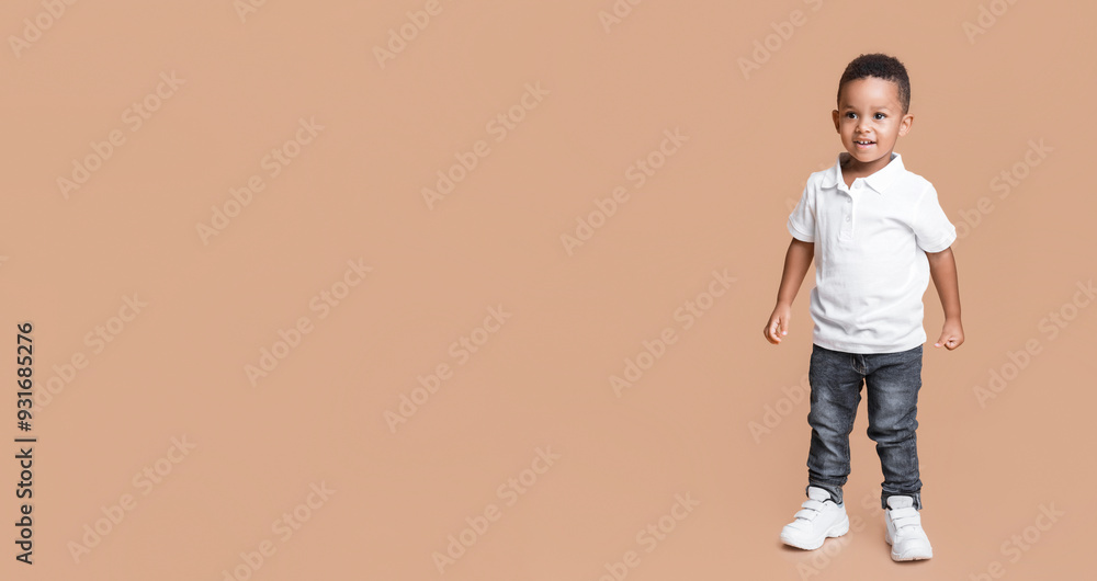 Full length portrait of smiling little black boy in jeans and white t-shirt on yellow studio background Full length portrait of smiling little black boy in jeans and white t-shirt on yellow studio background