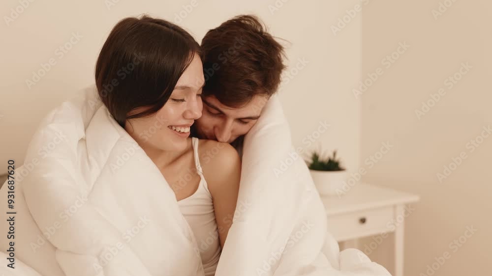 A loving couple wrapped in a duvet, embracing in bed, feeling in love in a cozy bedroom setting. A loving couple wrapped in a duvet, embracing in bed, feeling in love in a cozy bedroom setting.