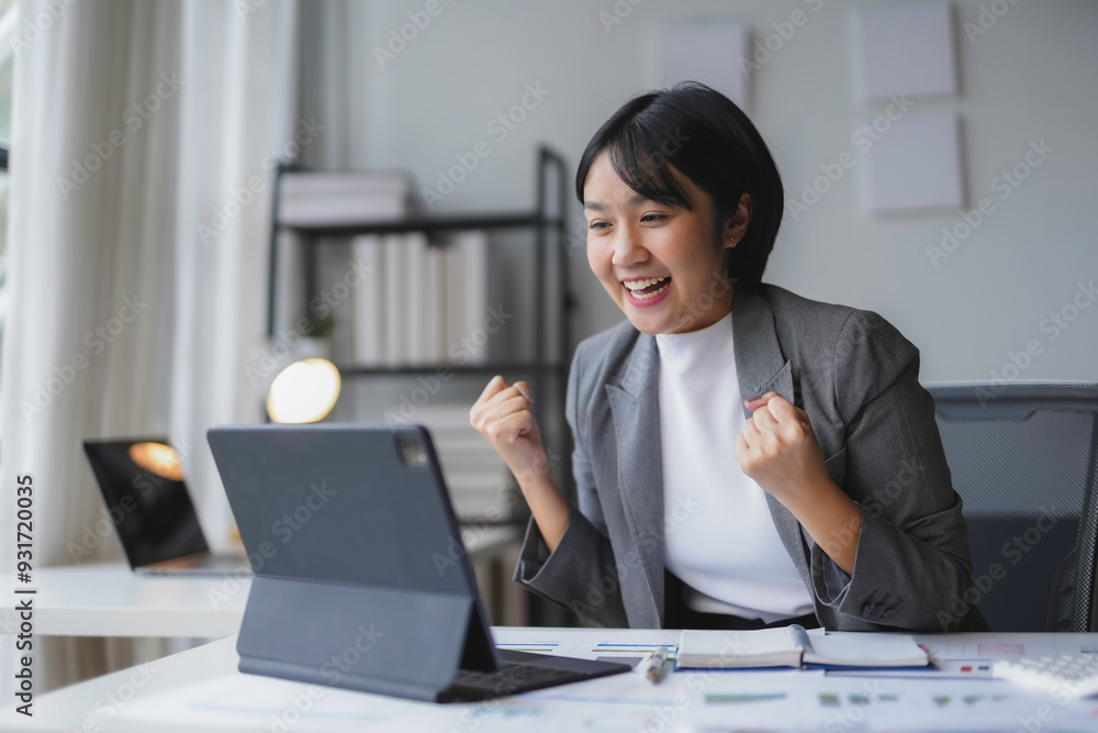 Young businesswoman is raising her fists in the air, feeling happy and excited about her success while working on a project in the office Young businesswoman is raising her fists in the air, feeling happy and excited about her success while working on a project in the office