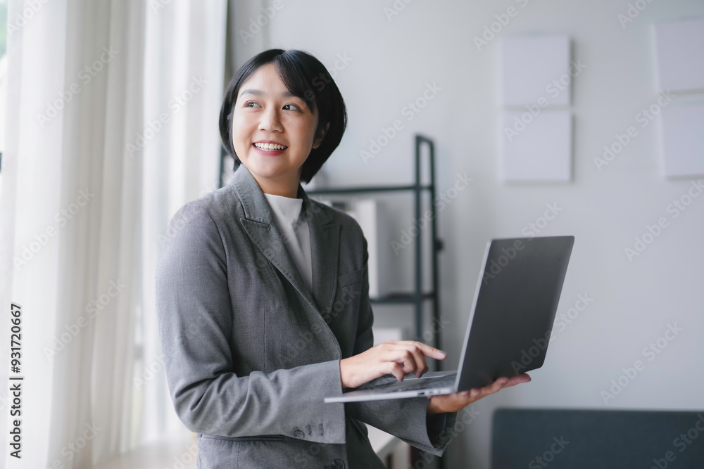 Young businesswoman is using a laptop and smiling while working from her office Young businesswoman is using a laptop and smiling while working from her office