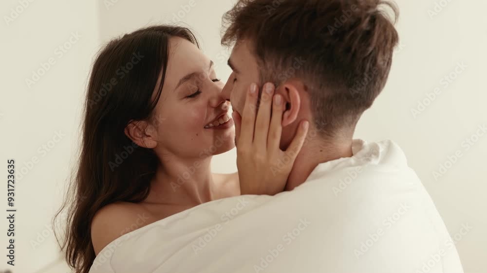 A loving couple engages in a tender embrace, exchanging smiles and affection under a warm blanket in bed A loving couple engages in a tender embrace, exchanging smiles and affection under a warm blanket in bed