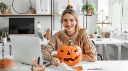 A woman is sitting at a desk with a pumpkin on it. She is smiling and holding the pumpkin. Halloween Concept