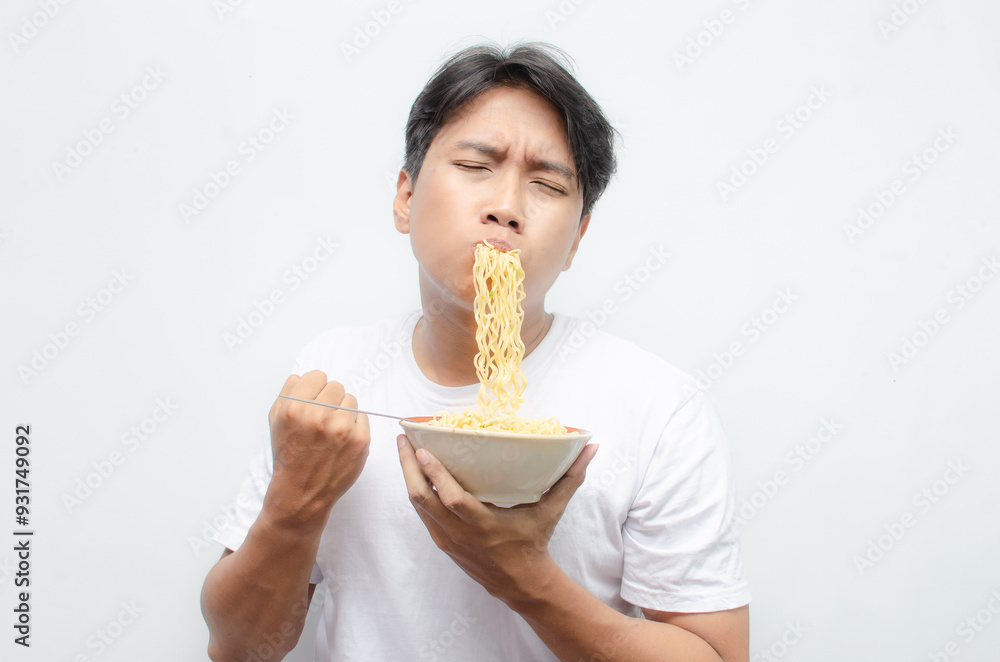 young asian man eats noodles. ecstatic young asian man with mouth full of noodles. young man in white tshirt enjoying noodles. young asian man eats noodles. ecstatic young asian man with mouth full of noodles. young man in white tshirt enjoying noodles.
