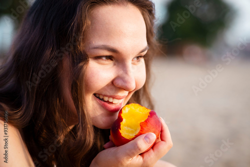 Foto Girl eats juicy peach on the beach. Ripe peach.