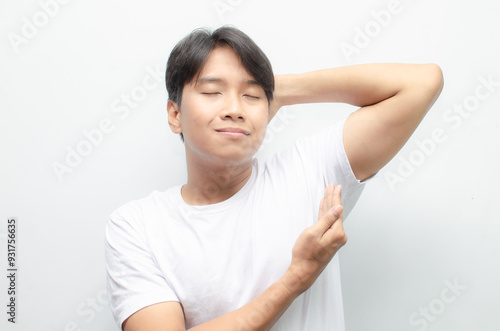 A young Asian man in white tshirt smells the freshness of his odor from armpit. Man enjoys his freshness and cleanliness. man smelling his armpit