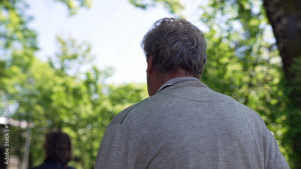Elderly man walking down a path in a park, surrounded by green trees and nature. back view shows him wearing a grey sweater, enjoying a peaceful and sunny day outdoors Elderly man walking down a path in a park, surrounded by green trees and nature. back view shows him wearing a grey sweater, enjoying a peaceful and sunny day outdoors
