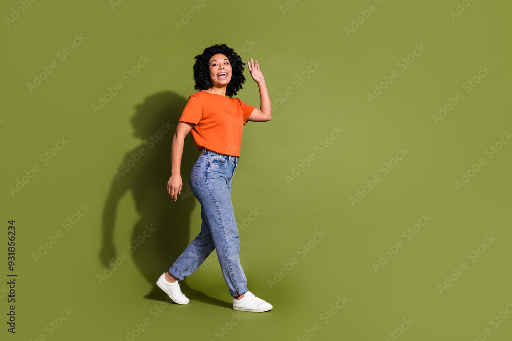 Full size photo of pretty young girl walking wave hand hello wear trendy orange outfit isolated on khaki color background Full size photo of pretty young girl walking wave hand hello wear trendy orange outfit isolated on khaki color background