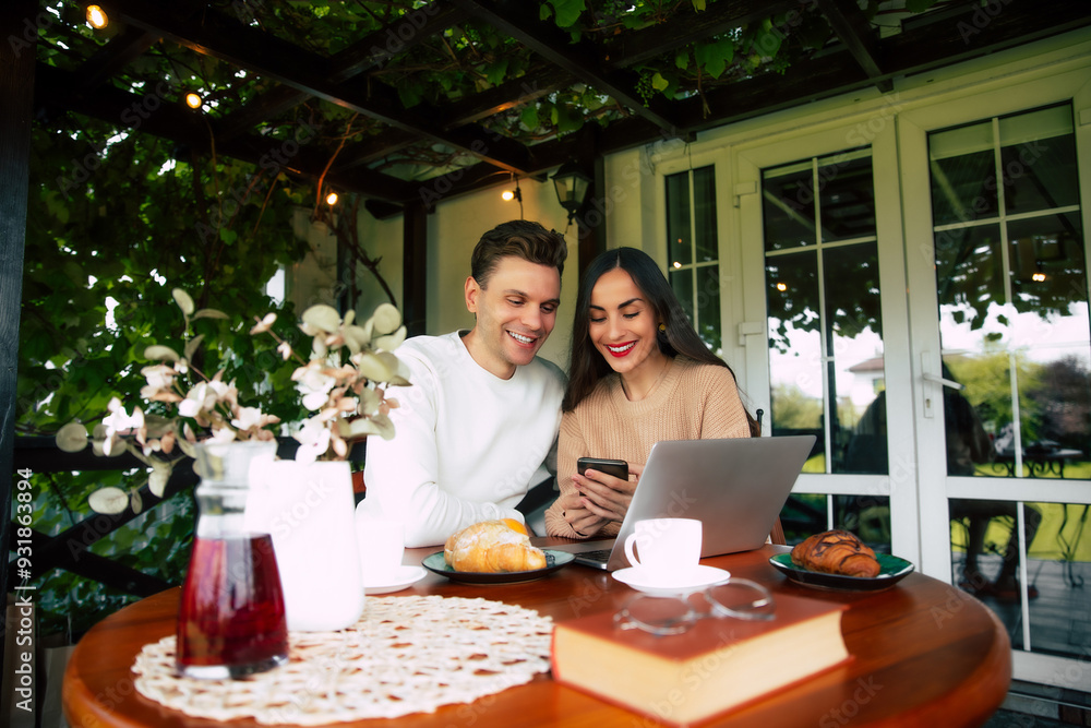 A joyful couple sharing a moment at a cozy café while browsing their phones and enjoying pastries in the bright afternoon light A joyful couple sharing a moment at a cozy café while browsing their phones and enjoying pastries in the bright afternoon light