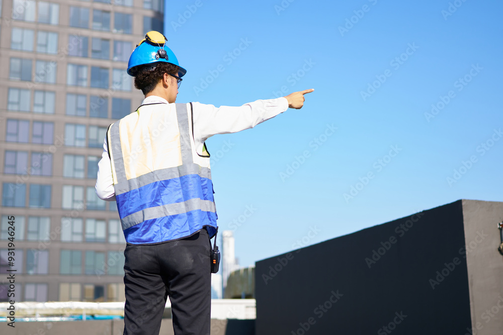 Back view engineer or worker pointing at high building on rooftop Back view engineer or worker pointing at high building on rooftop