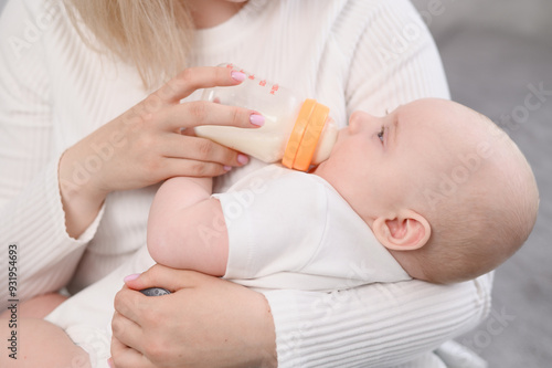 Family, motherhood and breastfeeding alternative concept. Close-up of woman feeding baby formula from plastic bottle. Baby enjoying nutritious meal