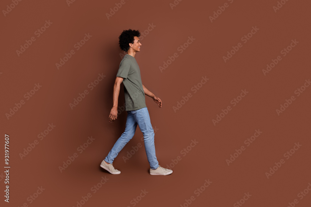 Side profile photo of youngster guy with wavy hair in gray t shirt and jeans walking showroom style clothing isolated on brown color background Side profile photo of youngster guy with wavy hair in gray t shirt and jeans walking showroom style clothing isolated on brown color background