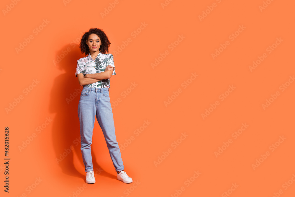 Photo of young attractive lady with brown wavy hair wearing jeans and hawaii shirt folded arms confident isolated on orange color background Photo of young attractive lady with brown wavy hair wearing jeans and hawaii shirt folded arms confident isolated on orange color background