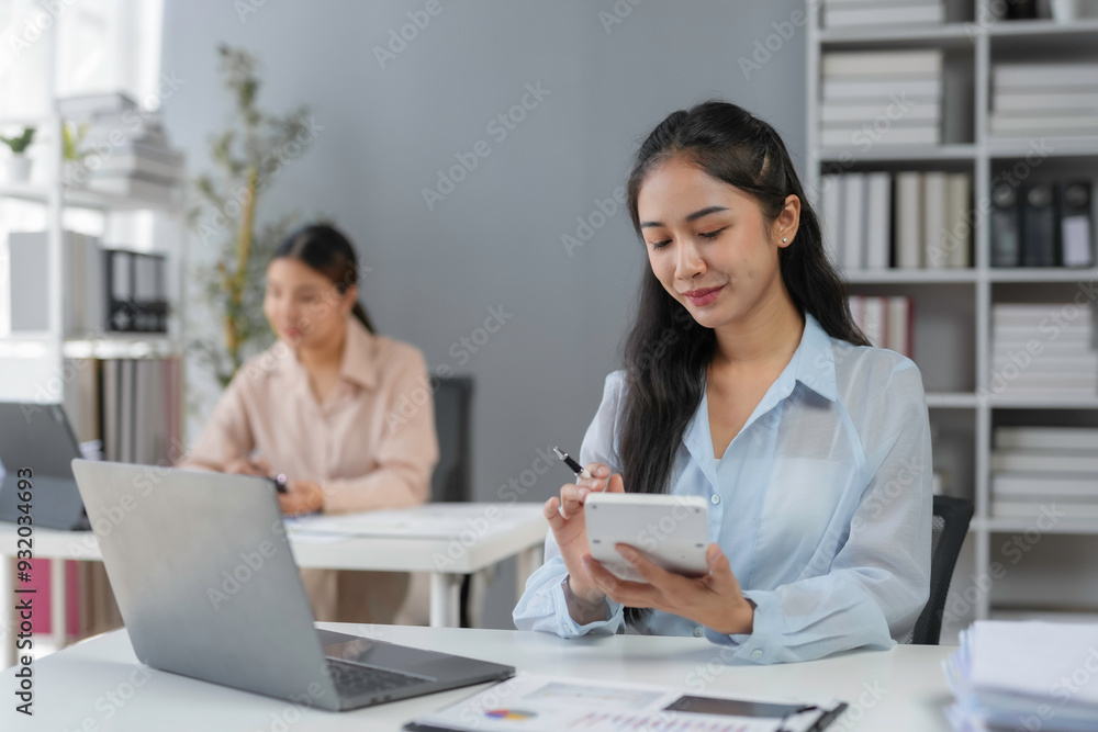Asian businesswoman is calculating financial data for a company using a calculator and a laptop computer at her office desk Asian businesswoman is calculating financial data for a company using a calculator and a laptop computer at her office desk