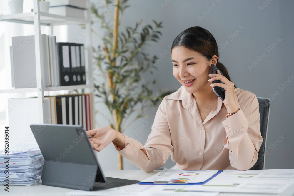 Smiling asian businesswoman working on a project in the office while participating in a phone call and using a digital tablet Smiling asian businesswoman working on a project in the office while participating in a phone call and using a digital tablet