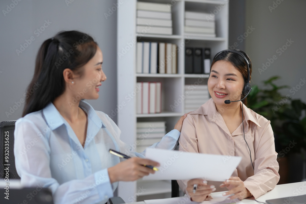 Manager comforting and assisting a smiling call center operator with a headset by giving her advice and instructions Manager comforting and assisting a smiling call center operator with a headset by giving her advice and instructions