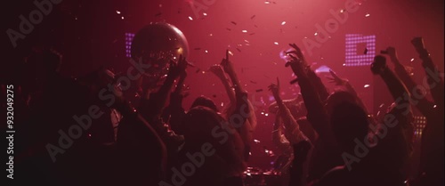 Extreme slow-motion shot of a group of people dancing happily with raised hands under falling confetti