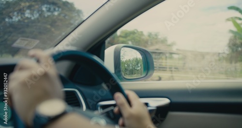 Close-up of hands gripping the steering wheel while driving through a scenic forested road