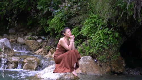  Secret Waterfall. An Asian girl in a brown dress against the backdrop of the tropics.