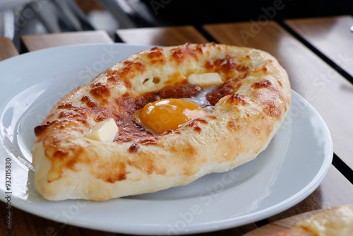 traditional Georgian bread with cheese, butter, egg known as adjaruli khachapuri plate in close up on table photo