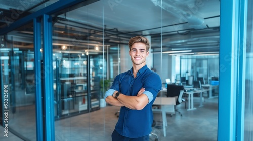 A cheerful young business leader, smiling with arms crossed, standing in a modern office with glass walls, bright lighting, and a clean, minimalist workspace. 