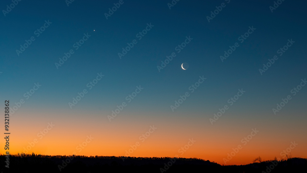 A crescent moon in and the north star in a vast blue sky at twilight with a burnt orange horizon above a silhouette of the land. Concepts of transition, the twilight of life , new day. Copy space. A crescent moon in and the north star in a vast blue sky at twilight with a burnt orange horizon above a silhouette of the land. Concepts of transition, the twilight of life , new day. Copy space.