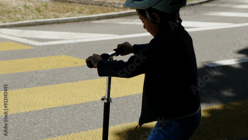 Boy riding scooter on street crosswalk, wearing blue pants and navy sweater, focusing on safe urban mobility, active outdoor lifestyle, and child-friendly transportation, sunny day in the city photo