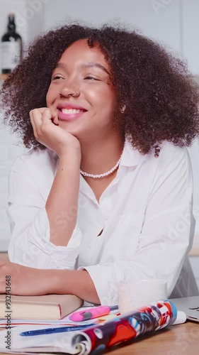 Young happy dreamy African American woman student fantasizing about successful future imagining job in large international corporation with high salary sits at table with textbooks. photo