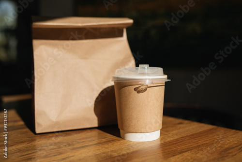 Close-up of a drink in a disposable take away cup next to a brown paper bag with take away food on a table