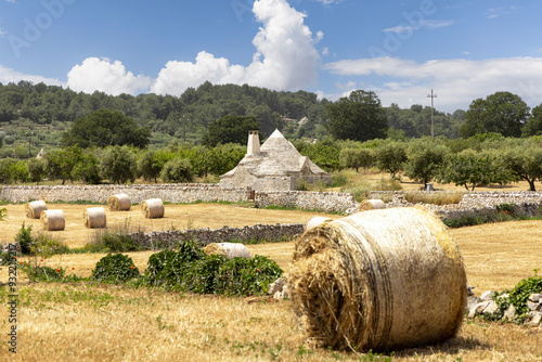 Picturesque view of the farm field after harvest, large straw bales and a trullo hut, Itria Valley (Valle d'Itria), Italy, Apulia