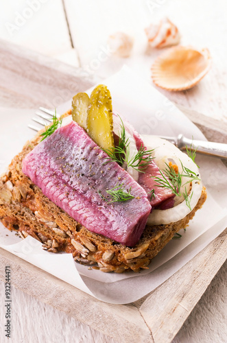 Traditional matie herring with onion rings and gherkins served as close-up on a rustic wholemeal bread photo