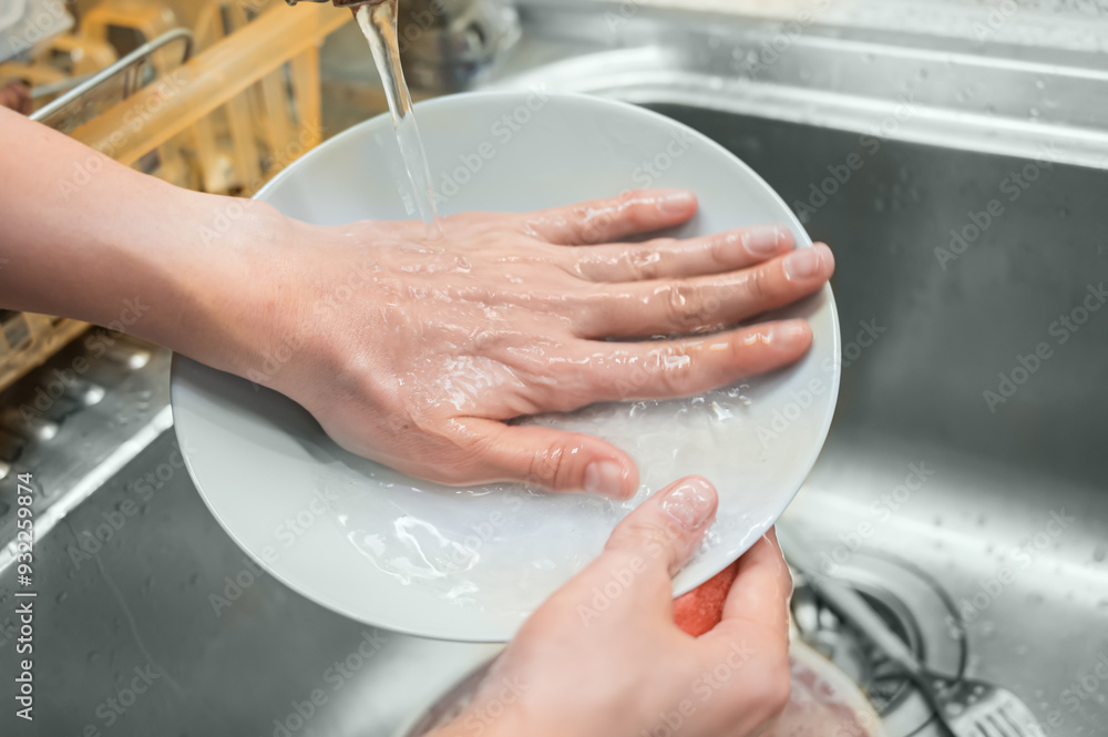 Girl washing dishes. Plate in hands under running water from tap close-up