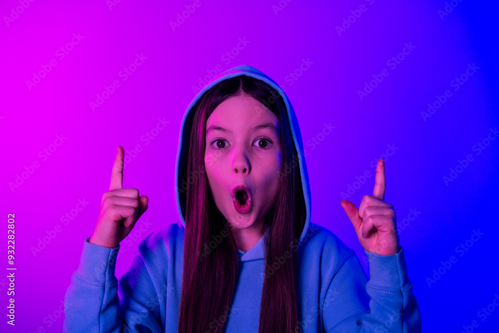 Obraz premium Photo of adorable impressed small girl wear hoodie pointing two fingers up empty space isolated magenta blue color background
