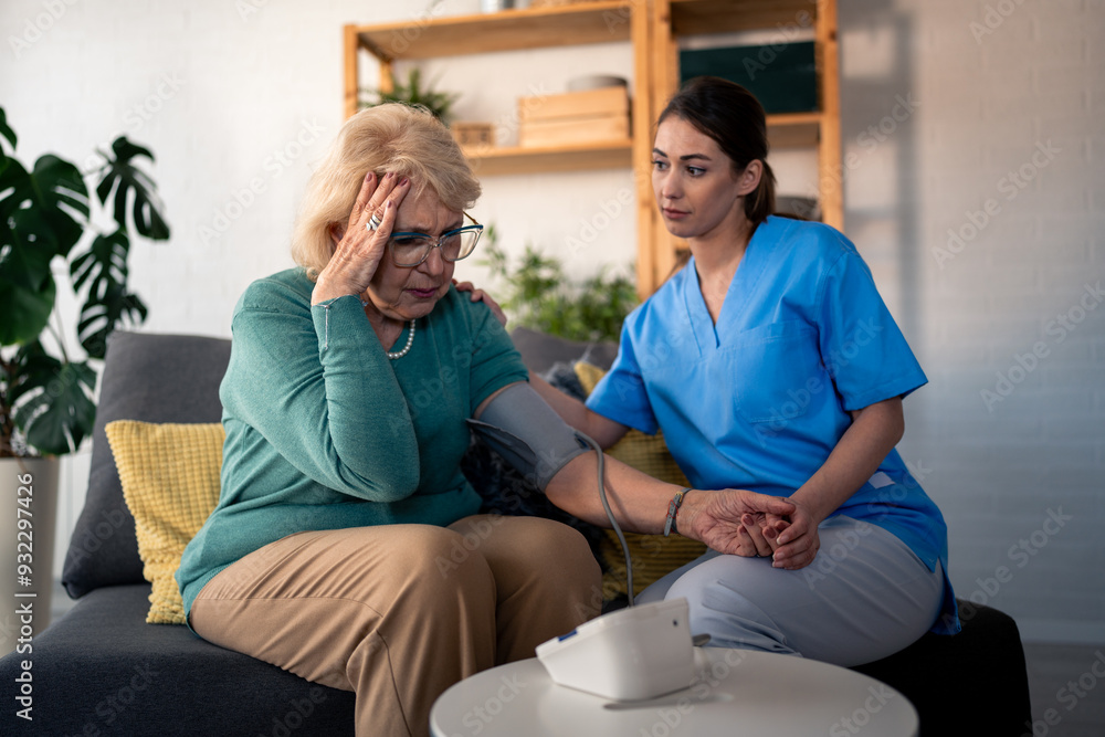 Obraz premium A female nurse in scrubs assists an elderly woman with her blood pressure check, providing medical care in a home setting, with a concerned look from the patient.