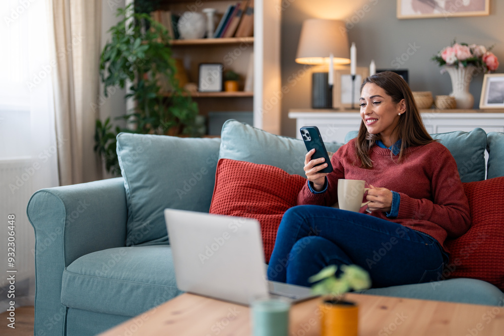 A focused woman multitasks in a cozy setting, engaging with her laptop and smartphone while relaxing on a sofa, a cup in hand suggesting a break. A focused woman multitasks in a cozy setting, engaging with her laptop and smartphone while relaxing on a sofa, a cup in hand suggesting a break.