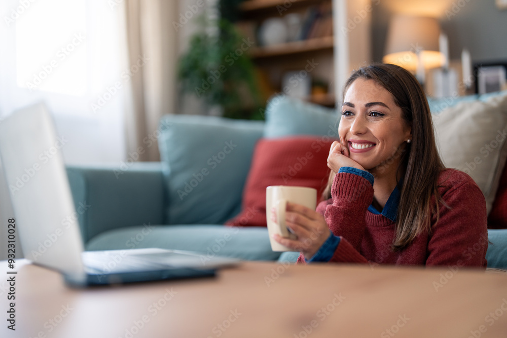 A smiling woman enjoys a video conversation, comfortably settled in her home's living room. Her casual attire and mug suggest a relaxed vibe during remote communication. A smiling woman enjoys a video conversation, comfortably settled in her home's living room. Her casual attire and mug suggest a relaxed vibe during remote communication.