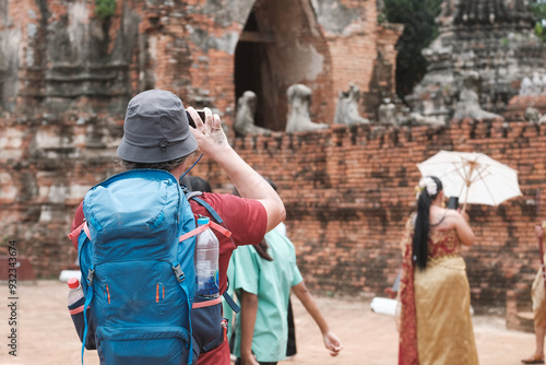 Tourist carrying backpacks and hats stand and take photos of an old temple with  smartphones