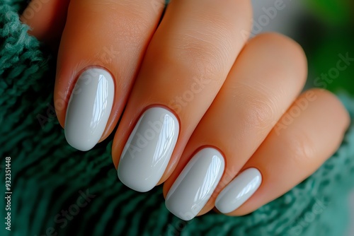 Stylish hand with elegant, light gray manicure showcasing smooth, glossy nails against a cozy green backdrop.