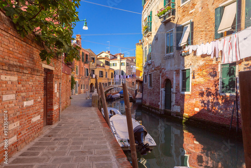 Schilderij op canvas A Venetian canal lined with brick buildings, a small boat, and laundry hanging a