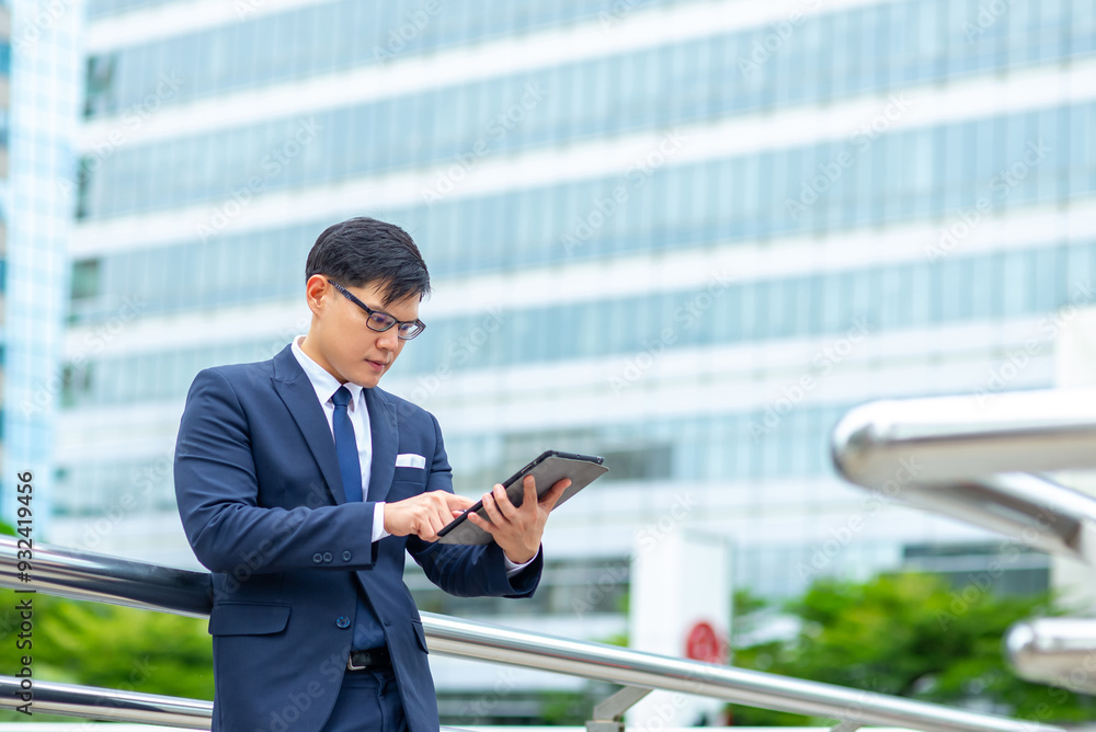 Confidence Asian businessman working on digital tablet during walking city street. Professional male executive using technology working corporate business financial and communication in the city. Confidence Asian businessman working on digital tablet during walking city street. Professional male executive using technology working corporate business financial and communication in the city.