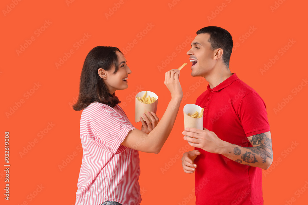 Young couple eating french fries on orange background Young couple eating french fries on orange background