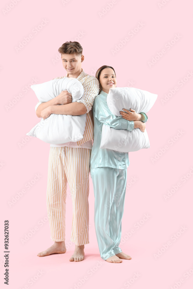 Young couple in pajamas with soft pillows on pink background Young couple in pajamas with soft pillows on pink background