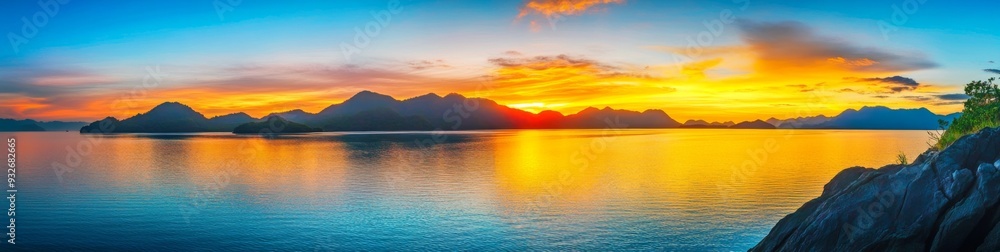 Naklejka premium Panoramic Sunrise Over Island with Mountains in Thailand Reflecting Vibrant Colors on Calm Waters, Peaceful Natural Beauty Scene