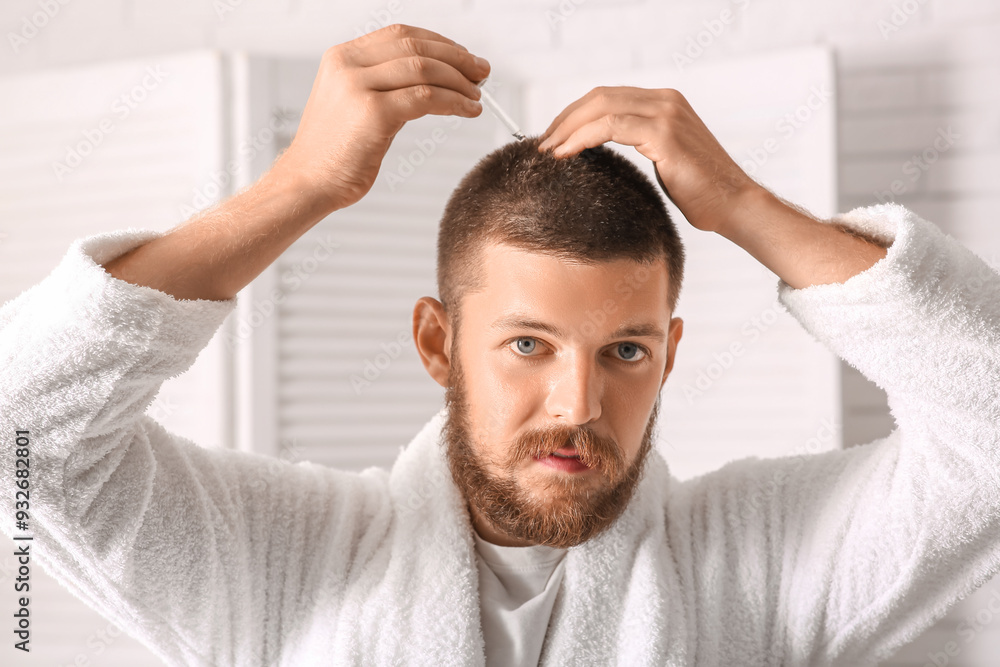Young man using serum for hair growth in bathroom. Hair loss concept Young man using serum for hair growth in bathroom. Hair loss concept