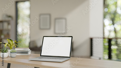 A laptop with a white-screen mockup on a wooden table in a contemporary home. home workspace