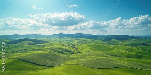 Lush green rolling hills stretch towards the horizon under a bright blue sky with clouds, offering a serene and picturesque landscape view