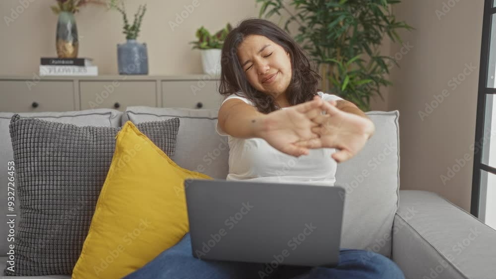 Woman relaxing on a sofa at home with a laptop, stretching her arms in ...